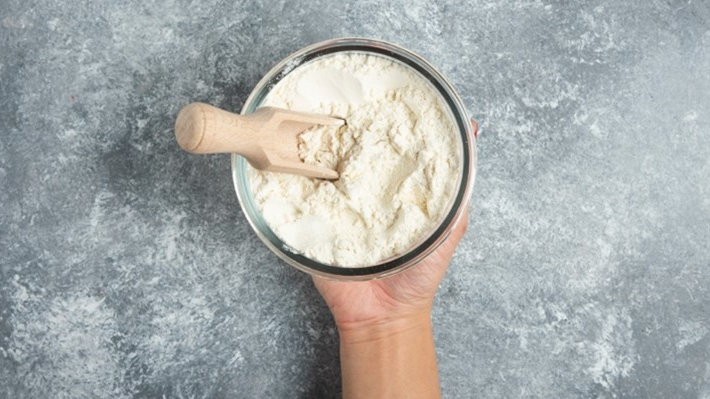 A picture of a container filled with powder with a wooden spoon