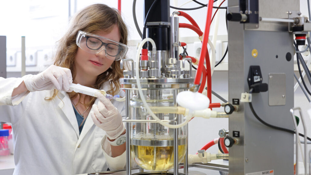 A female scientist take a sample out of a bioreactor 